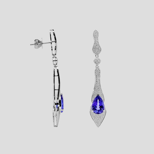 Pair of gold earrings with tanzanite blue gemstones on a light gray background