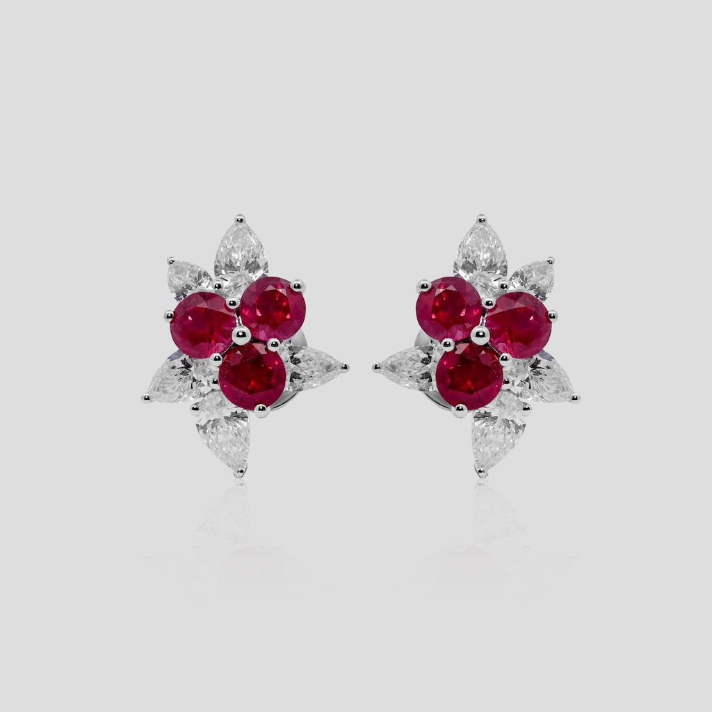 Pair of earrings with ruby red gemstones and diamond on a light gray background