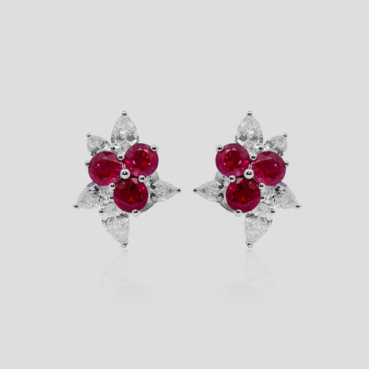 Pair of earrings with ruby red gemstones and diamond on a light gray background