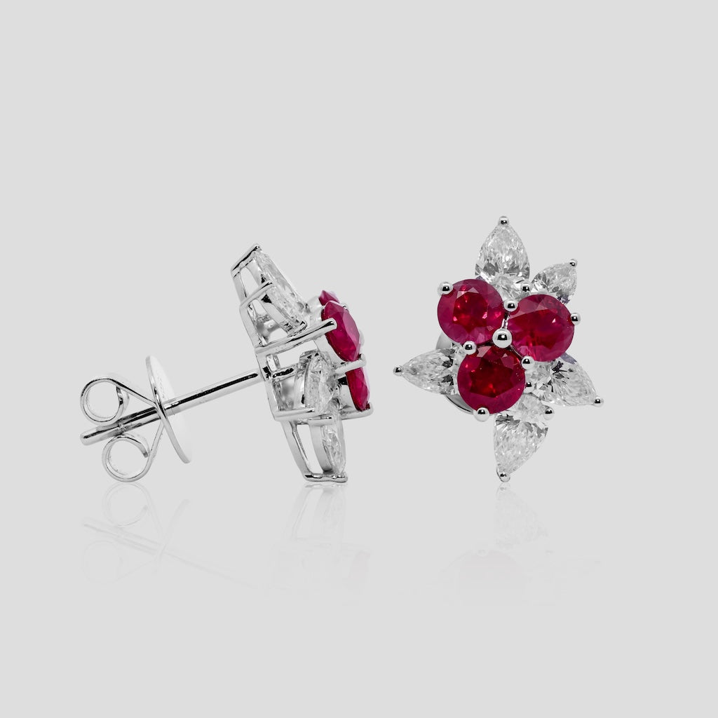 Pair of earrings with ruby red gemstones and diamonds on a light gray background