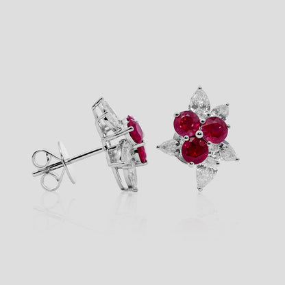 Pair of earrings with ruby red gemstones and diamonds on a light gray background