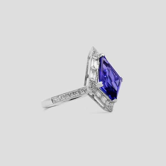 Ring with a kite shaped tanzanite gemstone and diamond accents on a light gray background