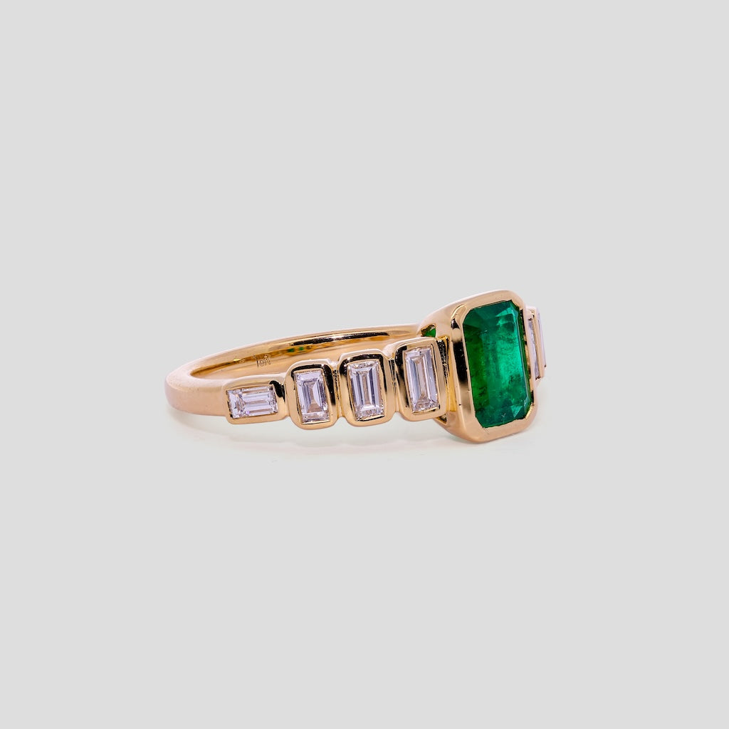 Gold ring with a emerald green gemstone and smaller diamonds on a light gray background