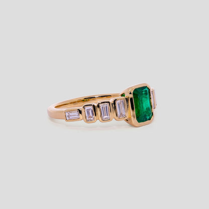 Gold ring with a emerald green gemstone and smaller diamonds on a light gray background