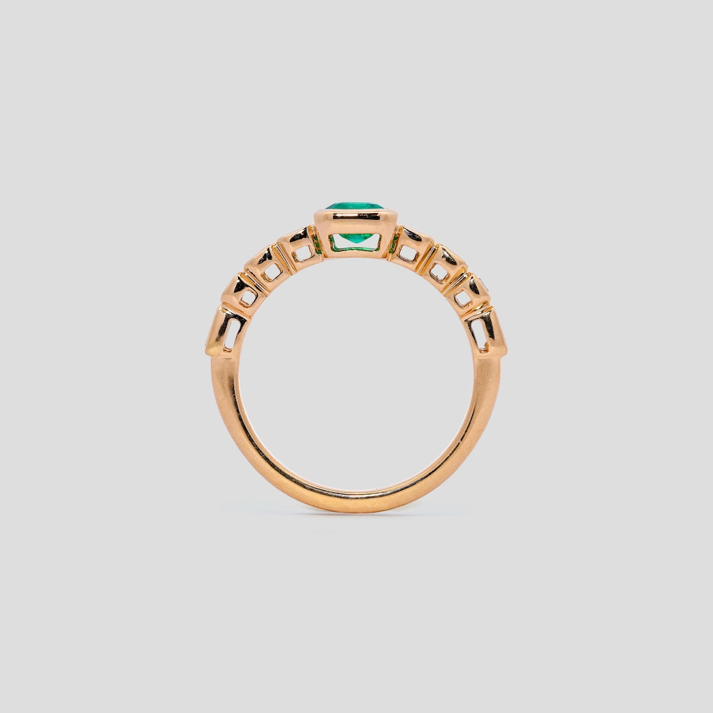 yellow gold ring with an emerald green gemstone on a light gray background