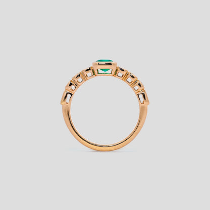 yellow gold ring with an emerald green gemstone on a light gray background