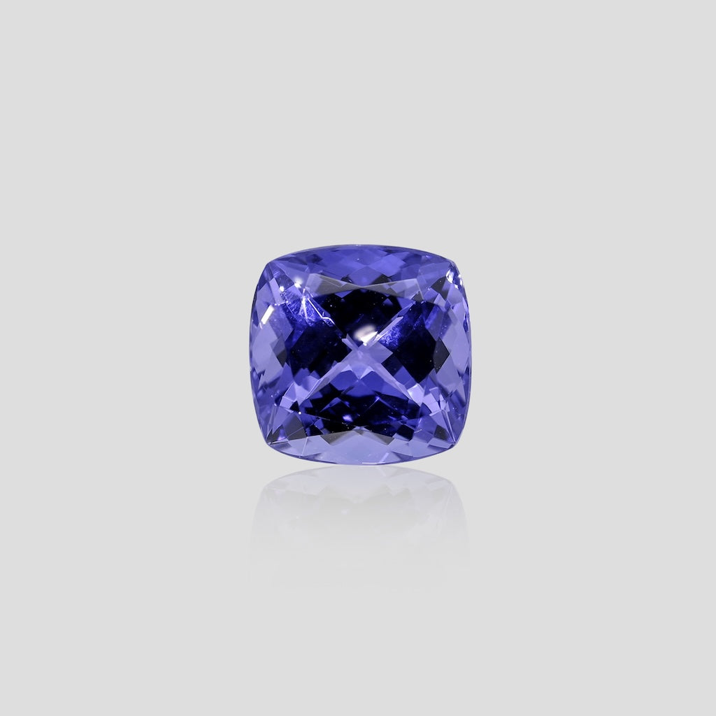 Cushion-shaped tanzanite blue gemstone on a light gray background
