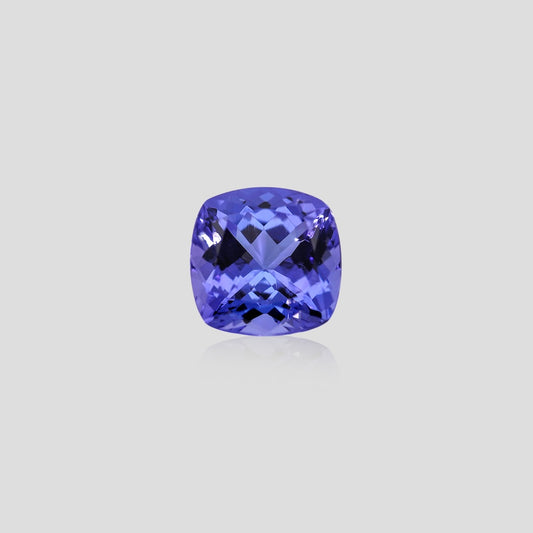 Cushion-shaped blue tanzanite gemstone on a light gray background