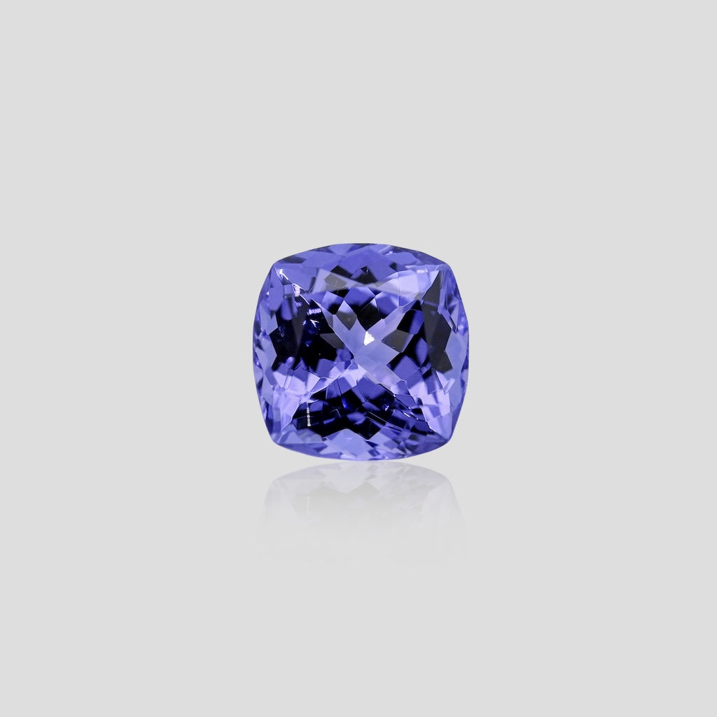 Cushion-shaped blue tanzanite gemstone on a light gray background