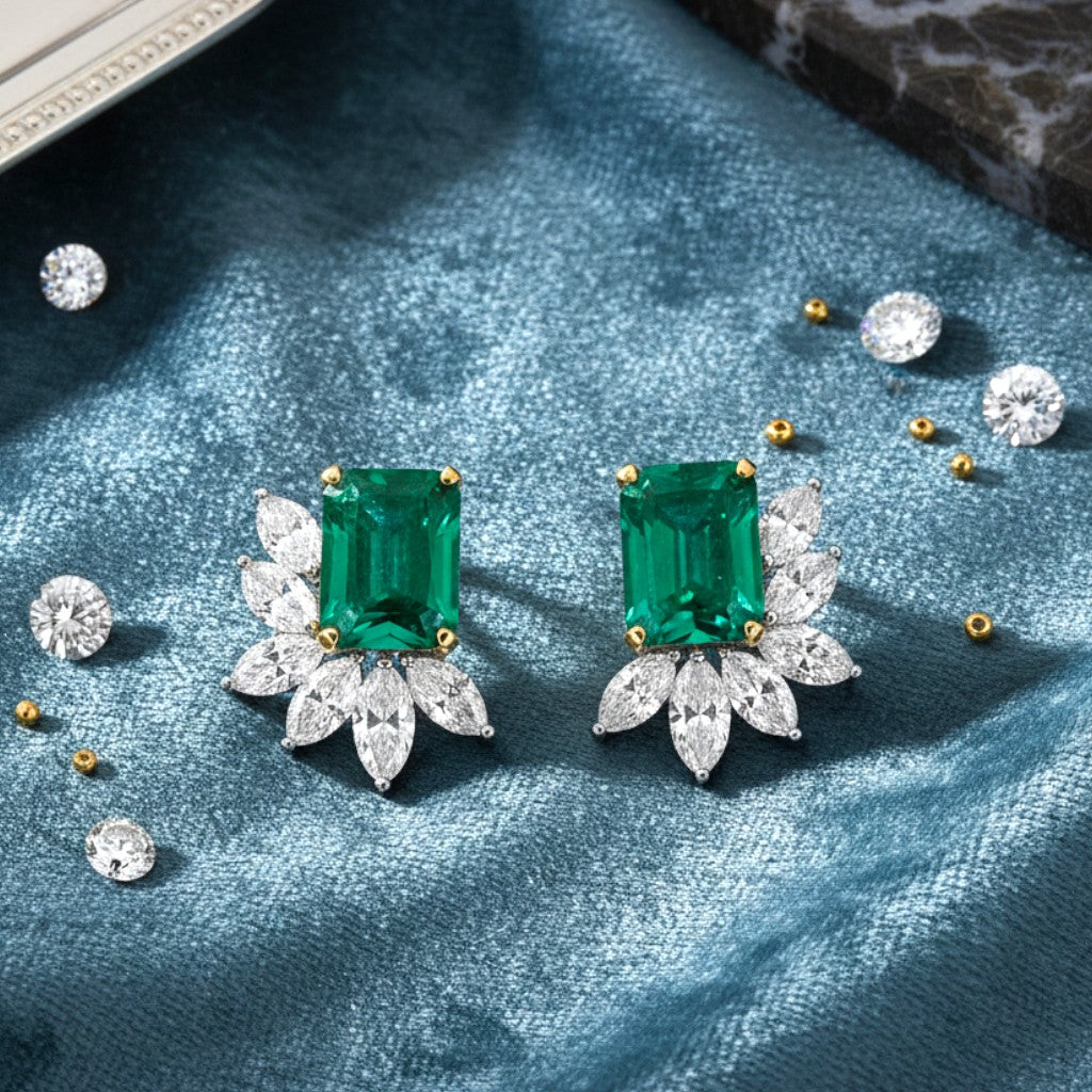 Luxury emerald jewellery earrings with floral designs on a blue fabric background.